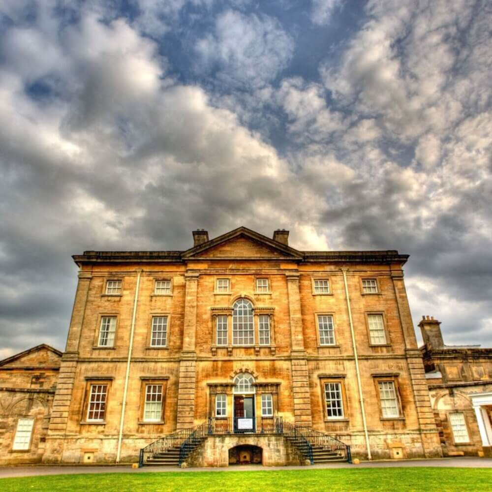 A historical stone mansion with ornate windows under a dramatic cloudy sky. - Home Instead