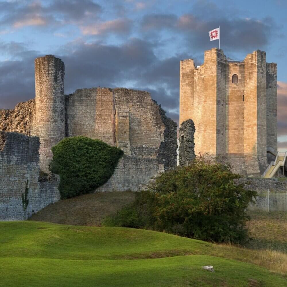 A stone castle with ruins and a tower flying a flag, set against a cloudy sky and lush green landscape. - Home Instead