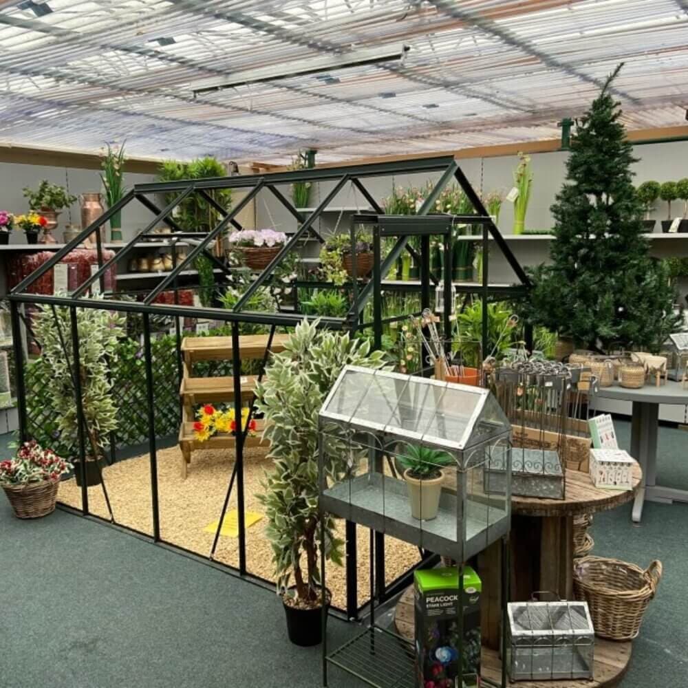 Indoor garden center with a small greenhouse, various plants, and gardening supplies displayed on shelves and tables. - Home Instead