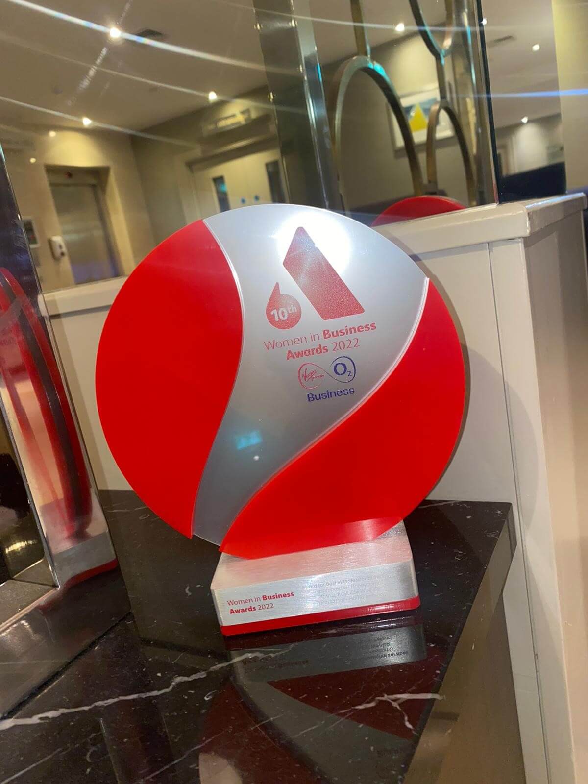 A red and silver "Women in Business Awards 2022" trophy displayed on a black marble surface. - Home Instead