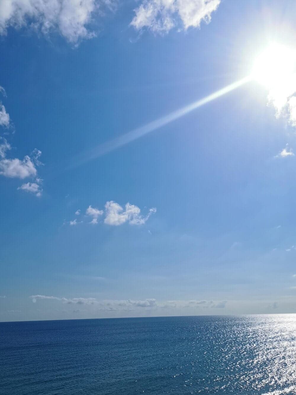 Bright sun over a calm ocean, with a few scattered clouds in the clear blue sky. - Home Instead