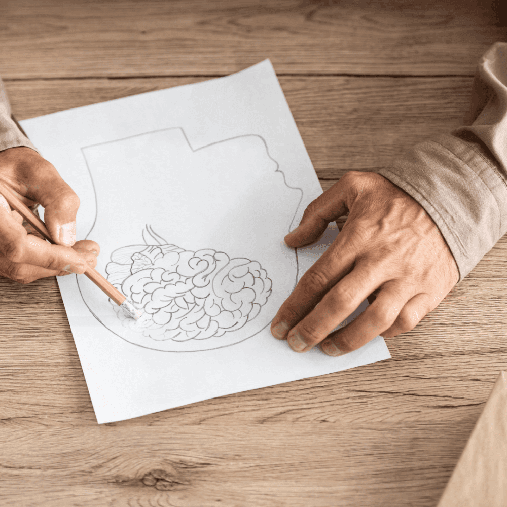 Person sketching a drawing of a brain on a white paper placed on a wooden table. - Home Instead