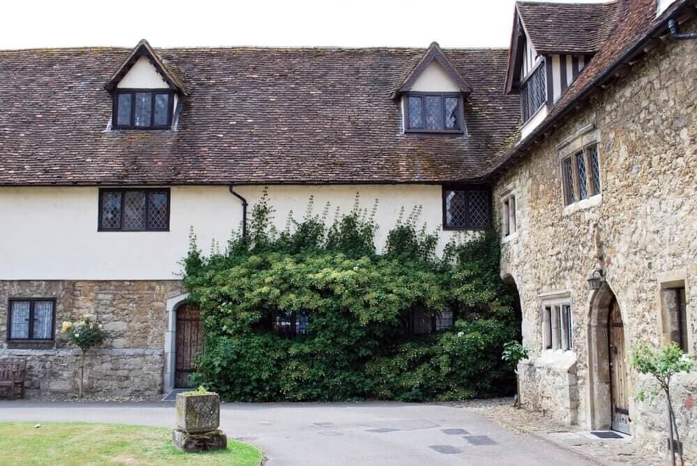 A charming stone house with a mix of stone and white walls, featuring climbing greenery and wooden windows. - Home Instead