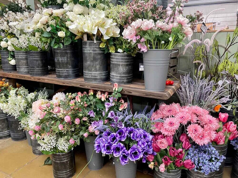 An assortment of colorful flowers in metallic pots displayed on wooden shelves in a flower shop. - Home Instead
