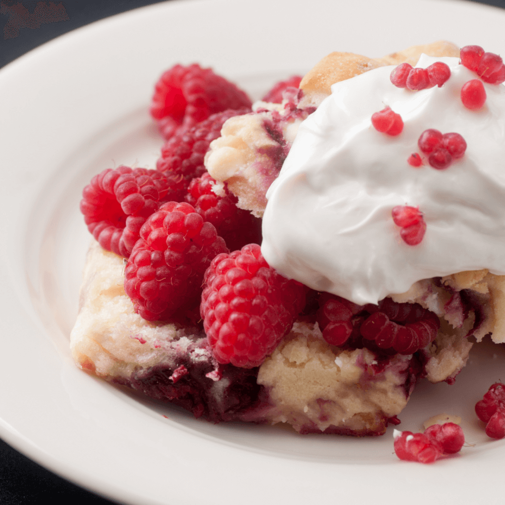 A dessert with fresh raspberries, whipped cream, and cake on a white plate. - Home Instead