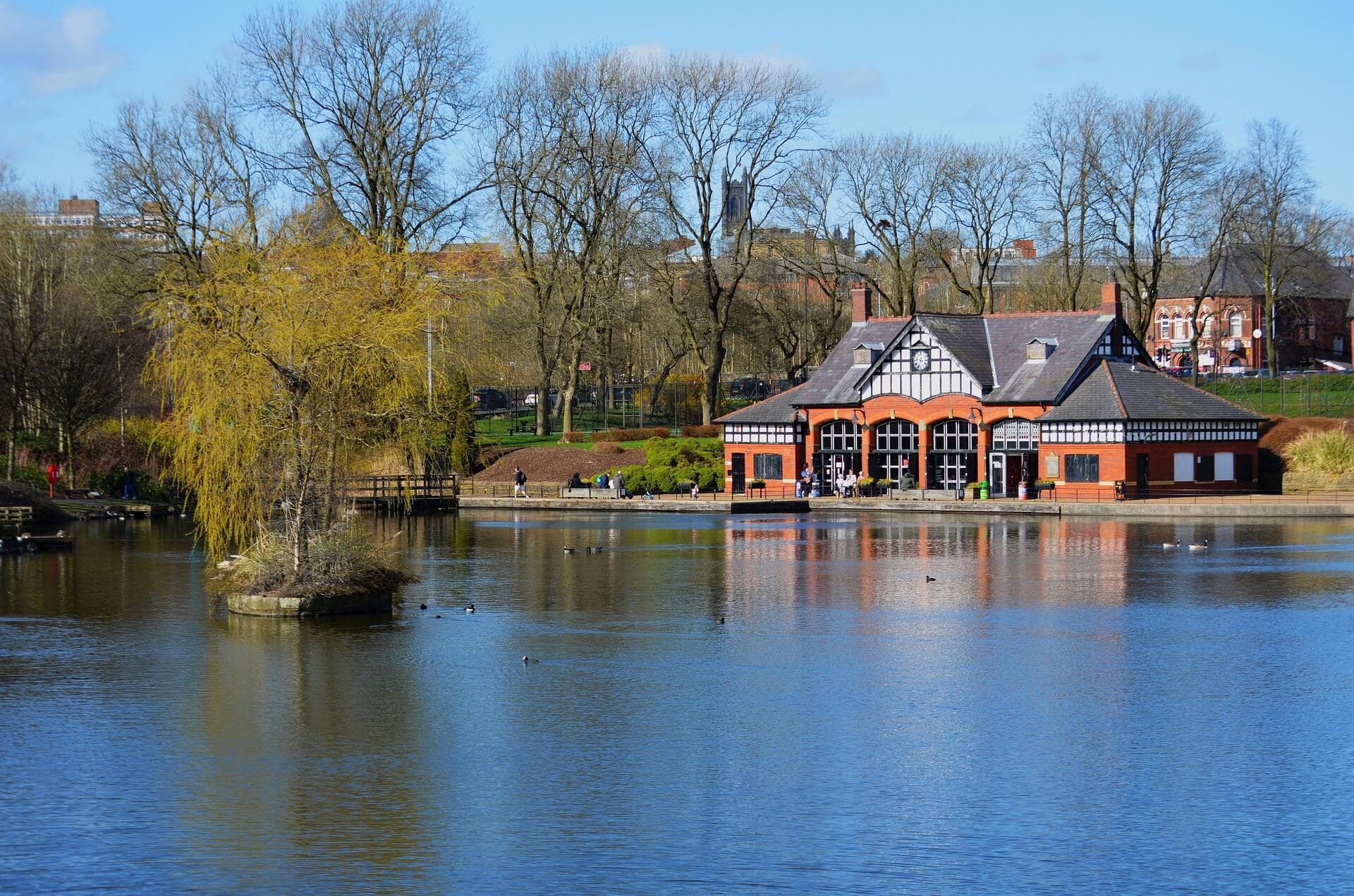 A red building with arched windows sits by a lake with bare trees and a small island on a sunny day. - Home Instead