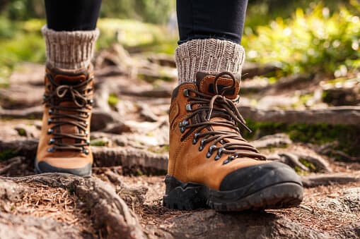 Close-up of a person wearing brown hiking boots and wool socks while walking on a forest trail. - Home Instead