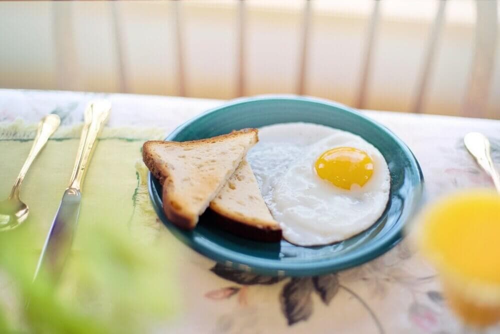Sunny-side up egg with toast on a green plate, set on a floral tablecloth with cutlery and a glass of juice. - Home Instead