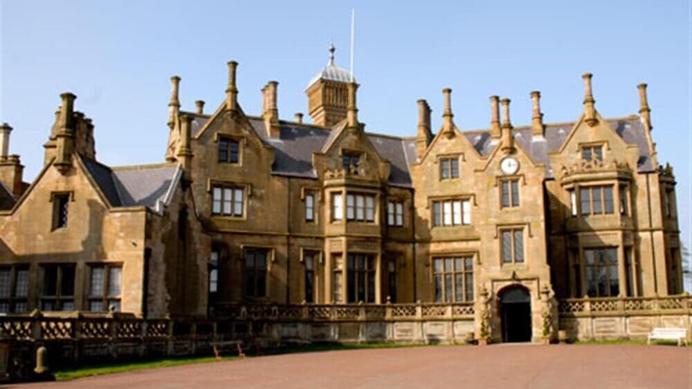 A historic, gothic-style mansion with multiple chimneys, prominent gables, and a central clock above the arched entrance. - Home Instead
