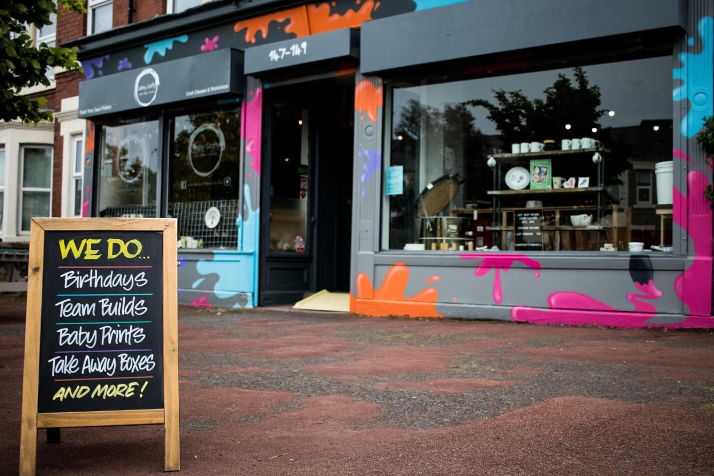 A colorful storefront with a chalkboard sign listing services: birthdays, team builds, baby prints, takeaway boxes, and more. - Home Instead