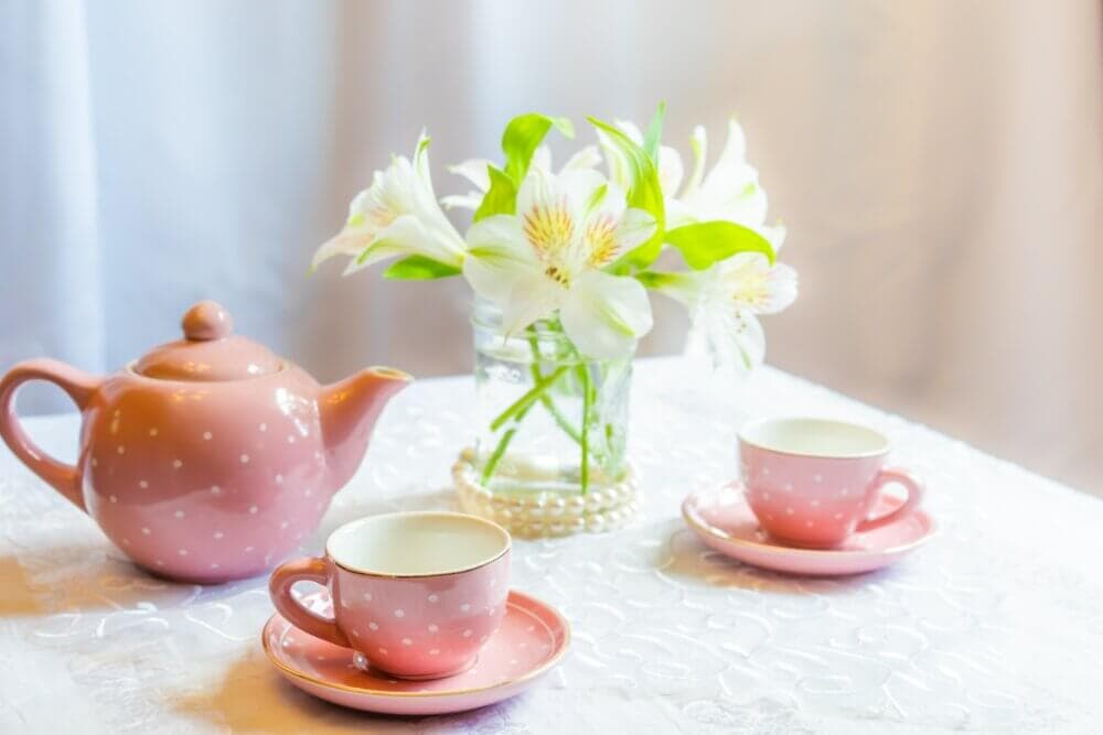 Pink teapot and matching teacups on a white tablecloth beside a vase of white flowers. - Home Instead