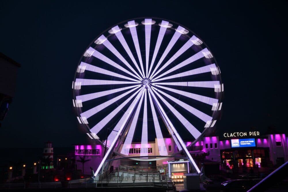 A brightly lit Ferris wheel at night near Clacton Pier, glowing with purple lights. - Home Instead