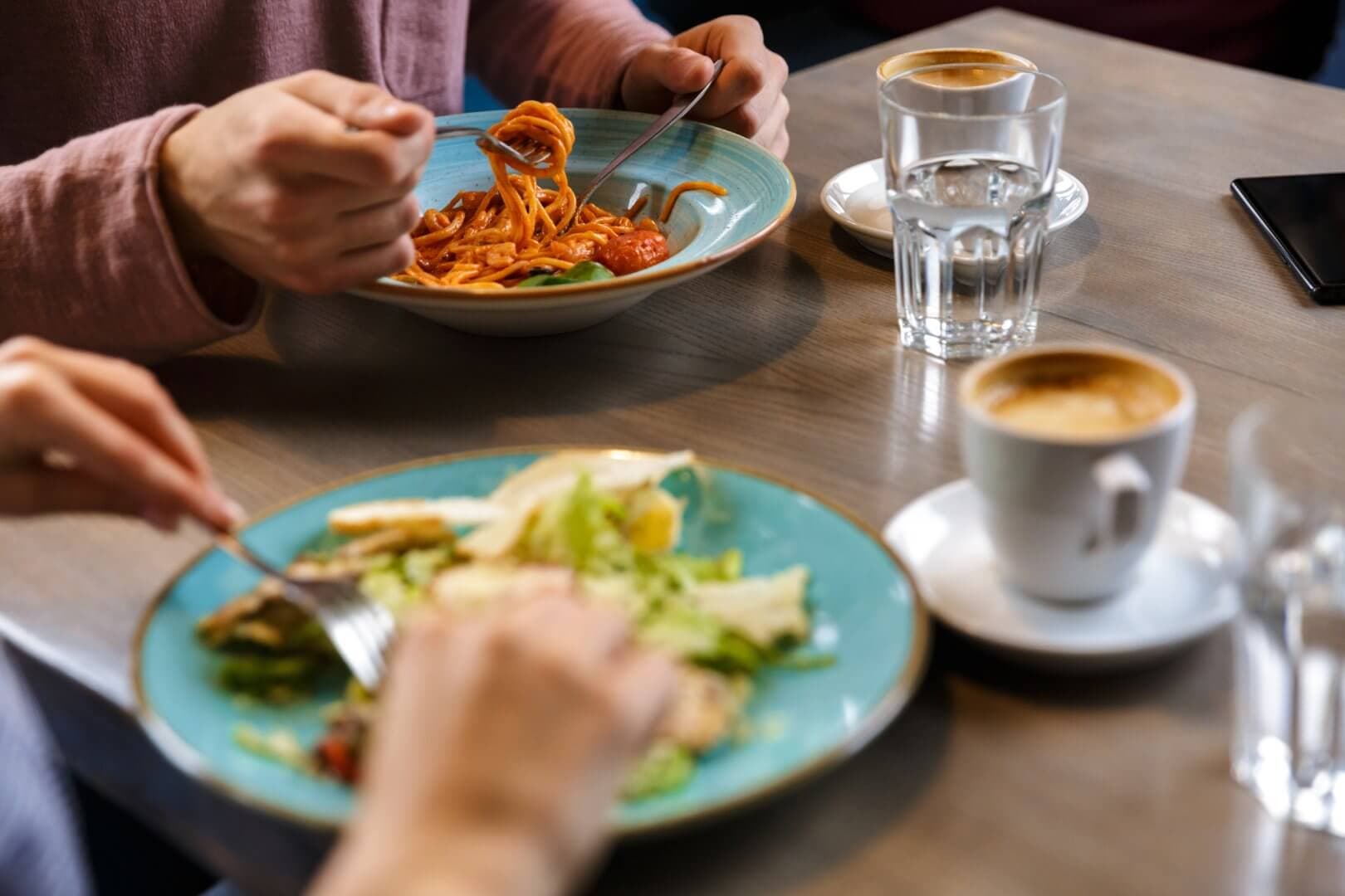 People eating pasta and salad at a table with glasses of water and cups of coffee. - Home Instead
