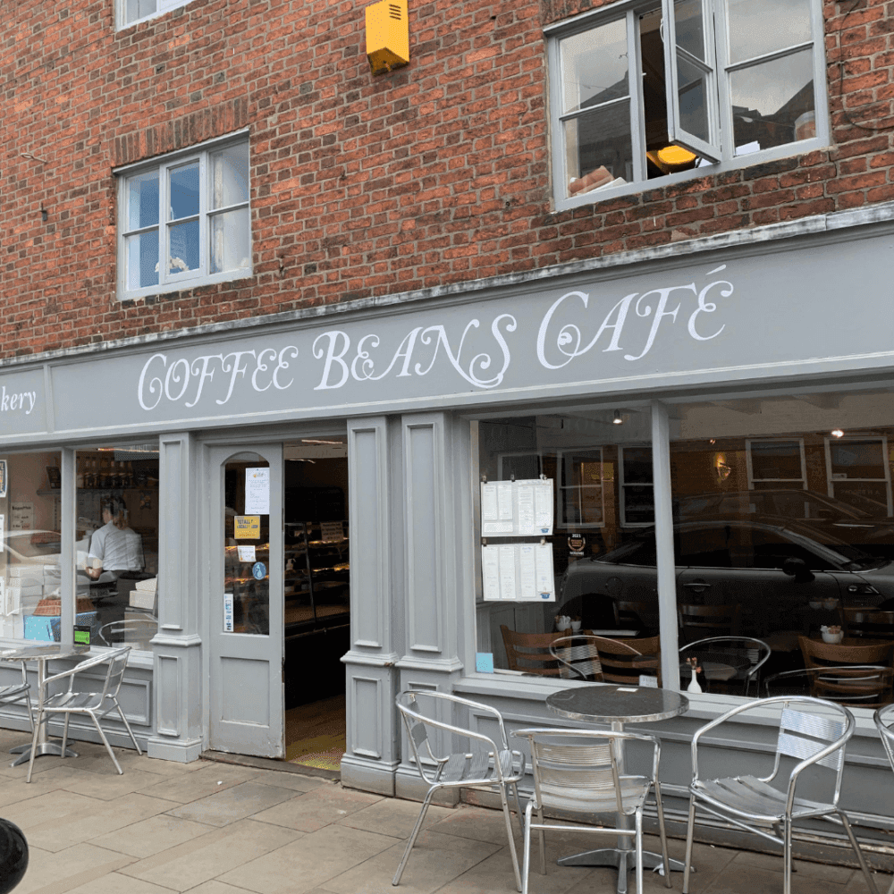Storefront of Coffee Beans Cafe with outdoor seating and large windows displaying the interior. - Home Instead
