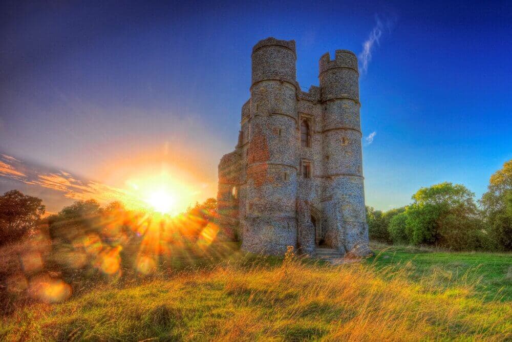 Sunset over a historic stone castle with cylindrical towers, surrounded by grassy fields and trees. - Home Instead