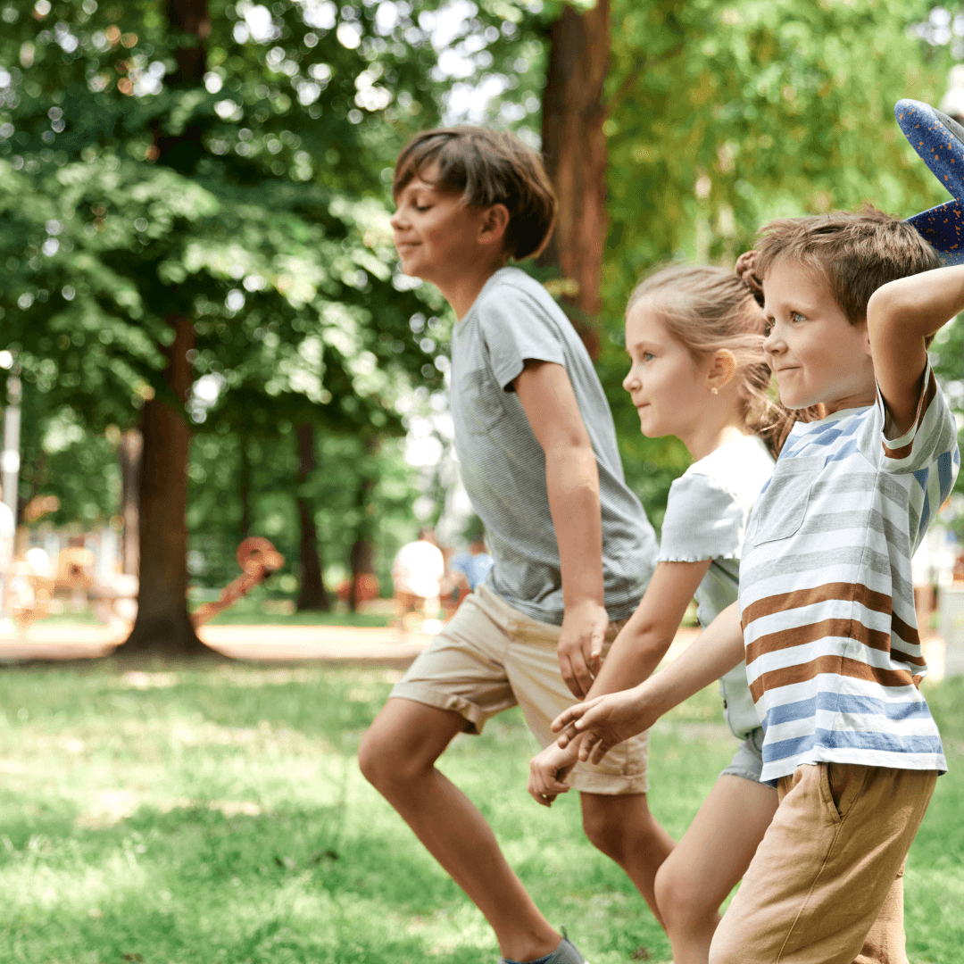 Three children happily running and playing in a lush green park on a sunny day. - Home Instead