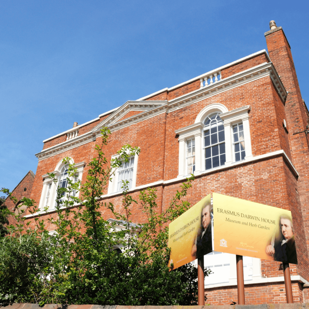 Erasmus Darwin House, a red-brick building with large windows, and a sign advertising the museum and herb gardens. - Home Instead