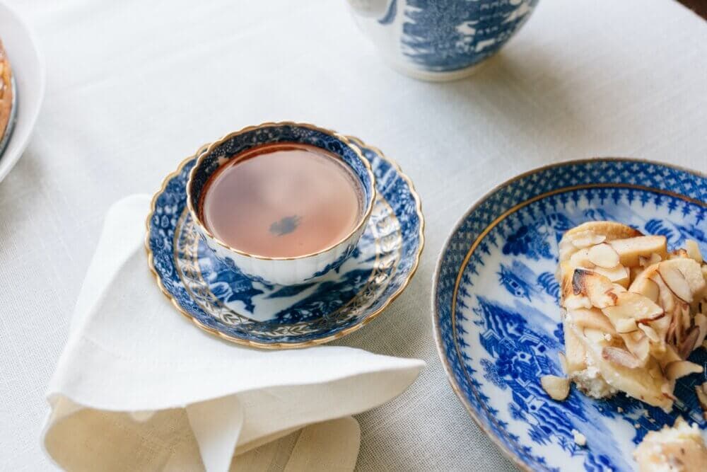 A cup of tea and a slice of almond cake sit on a white tablecloth, both in blue and white patterned dishes. - Home Instead
