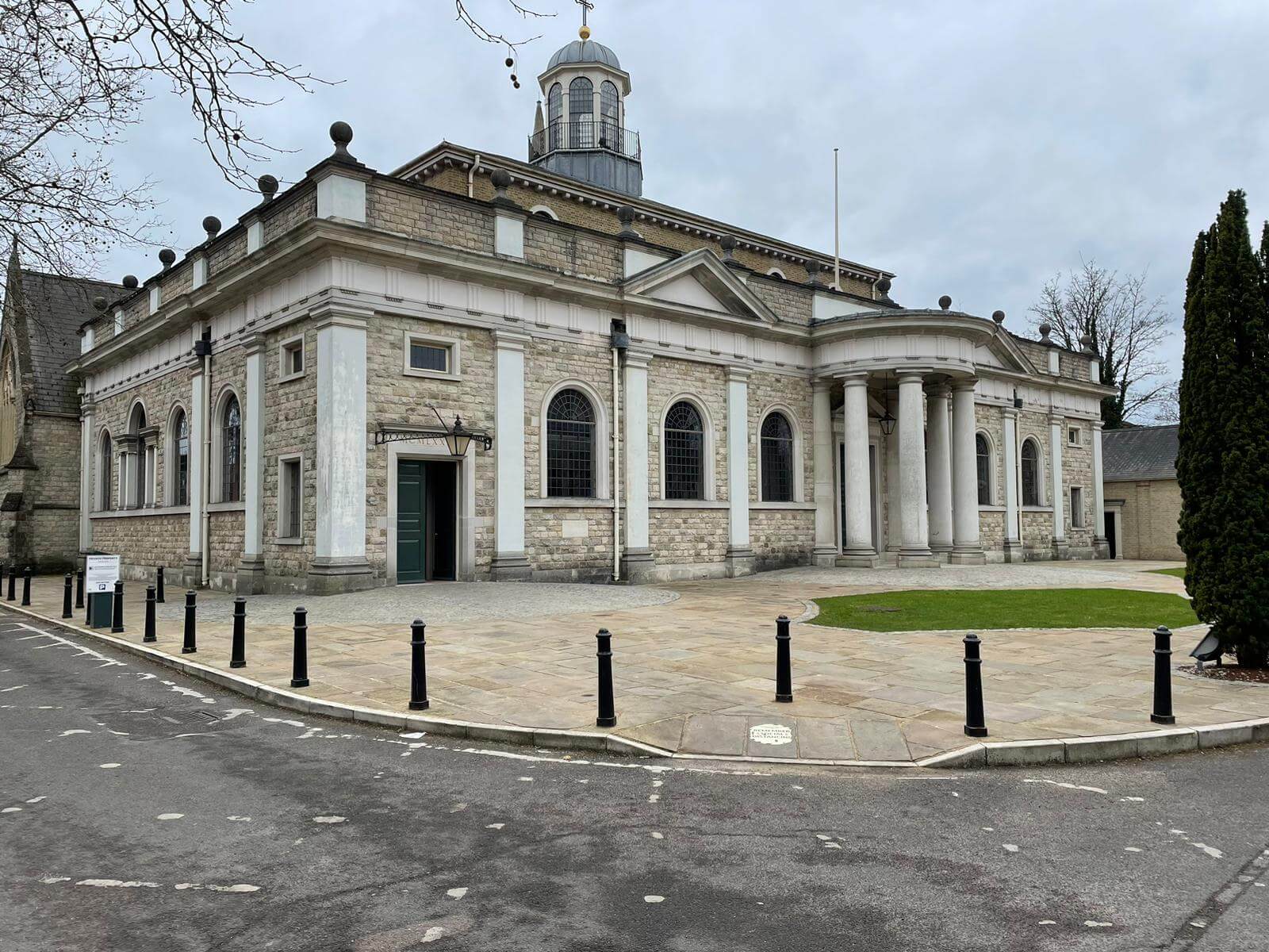 A historic stone building with columns and a dome, surrounded by bollards and a paved area with some grass. - Home Instead
