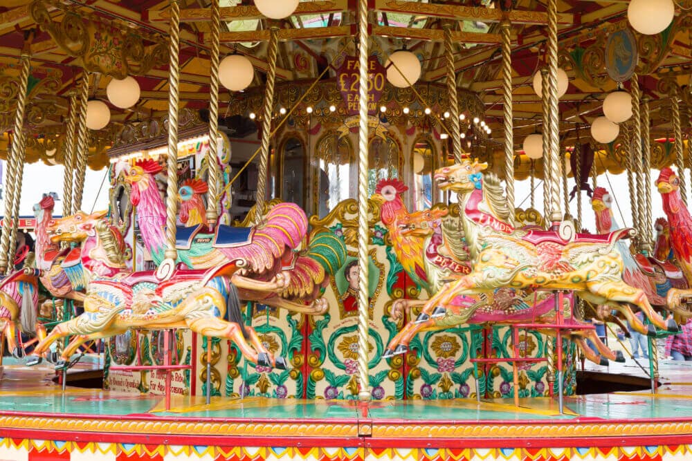 A colorful carousel with ornate, brightly painted horses and lights at a fairground. - Home Instead