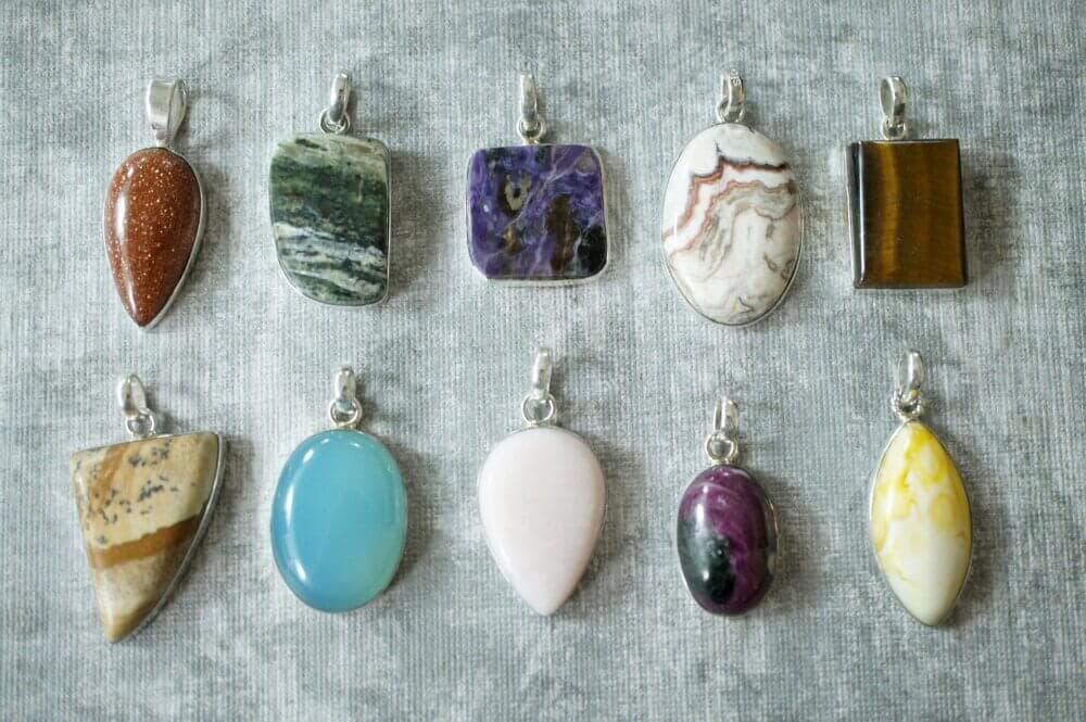 Ten gemstone pendants of various shapes and colors arranged in two rows on a gray textured background. - Home Instead