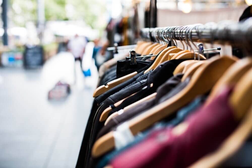 Close-up of clothes hanging on wooden hangers on a rack, an outdoor market setting in the background. - Home Instead