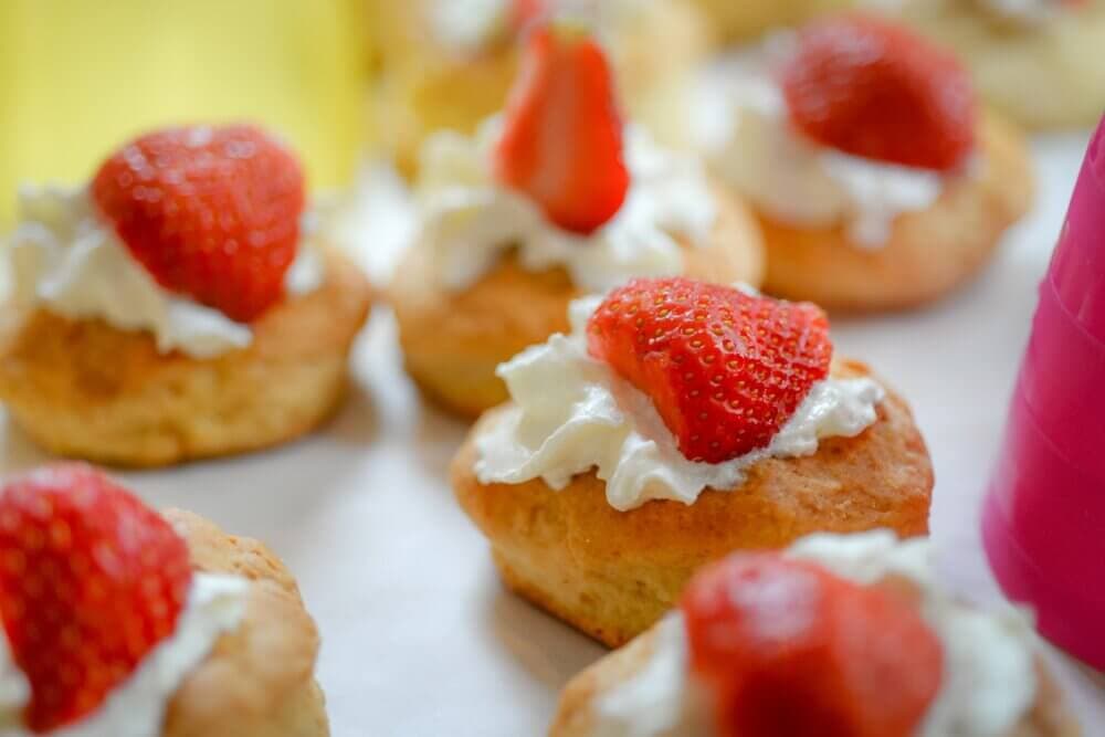 Close-up of pastries topped with whipped cream and fresh strawberries, arranged on a lined tray. - Home Instead