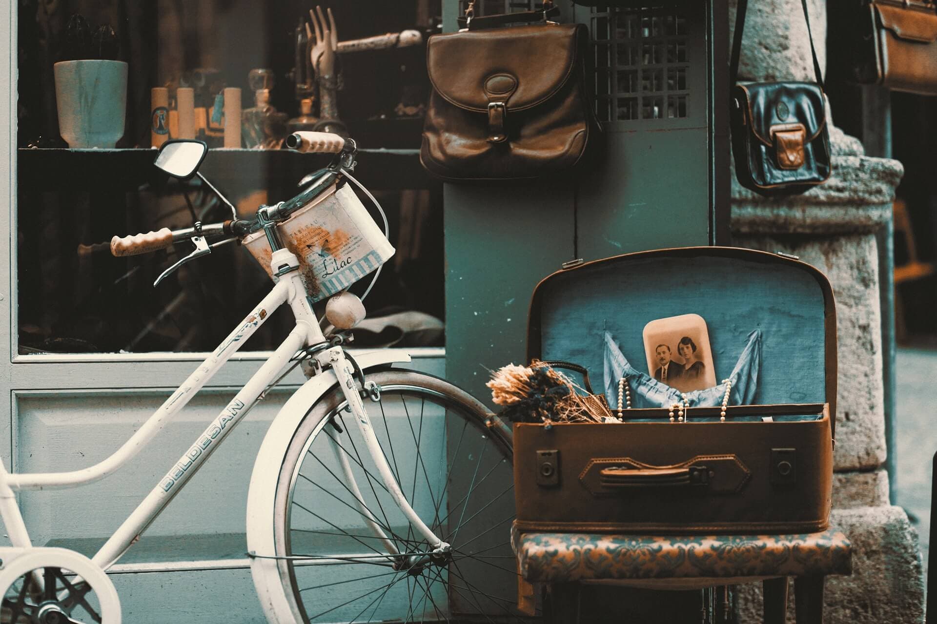 Vintage bicycle and leather bags displayed outside a store, with an open suitcase containing dried flowers and photographs. - Home Instead