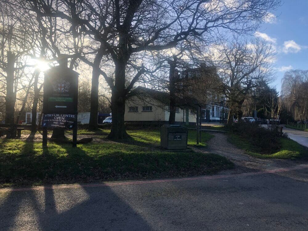 A sunlit park with a visitor center, tall bare trees, and a gravel path leading to a distant building. - Home Instead