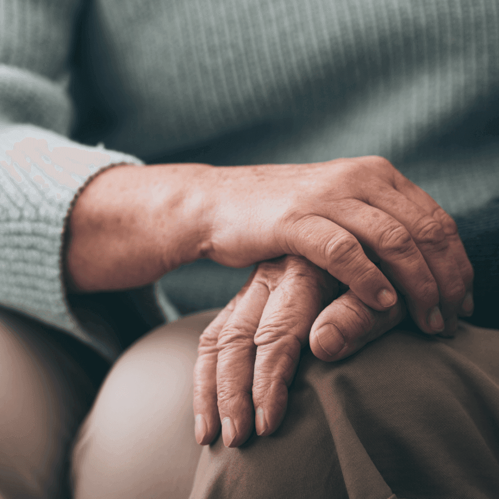Close-up of an elderly person’s hands, one resting gently on the other, both resting on their lap. - Home Instead