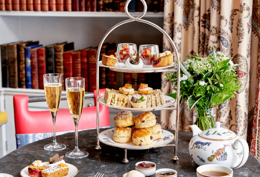 Elegant afternoon tea setup with a multi-tiered tray of pastries, sandwiches, and scones, alongside flowers and champagne. - Home Instead