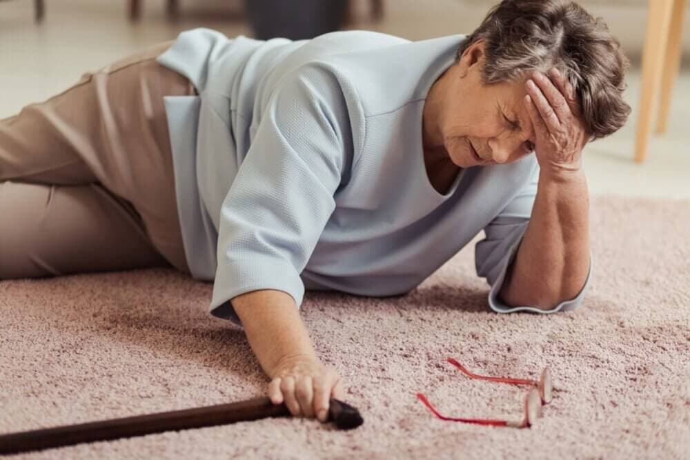 Elderly person on the floor, hand on head, holding a cane, with glasses resting nearby on the carpet. - Home Instead