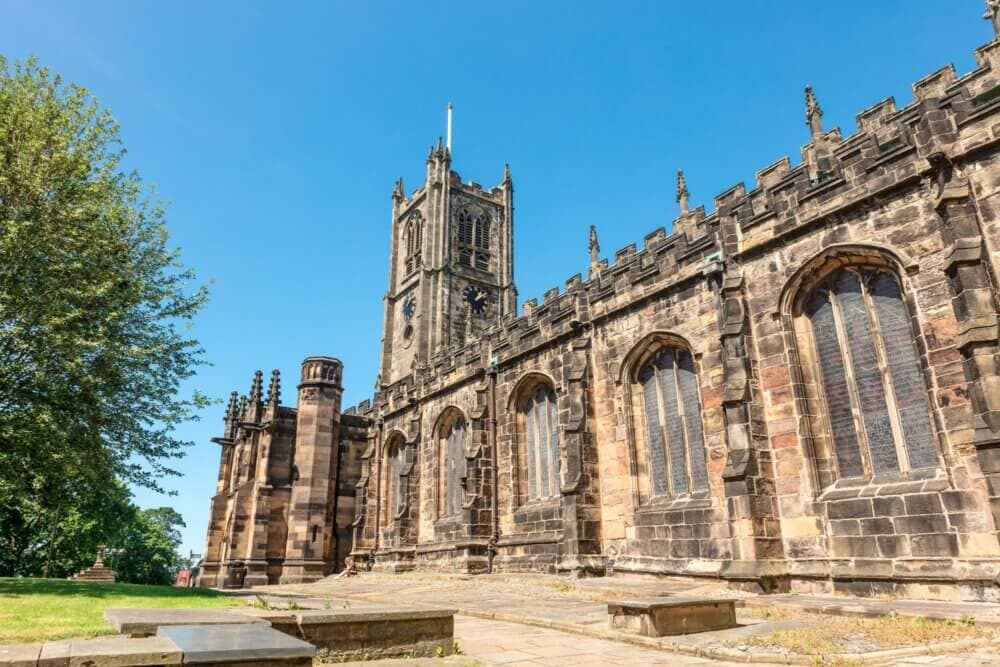 Historic stone church with arched windows and a tall clock tower against a clear blue sky. - Home Instead