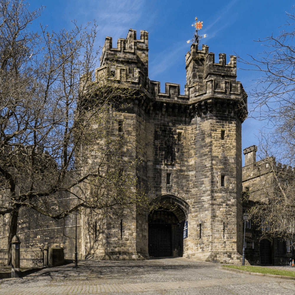A historic stone castle with two tall, crenellated towers and a central arched entrance under a clear blue sky. - Home Instead