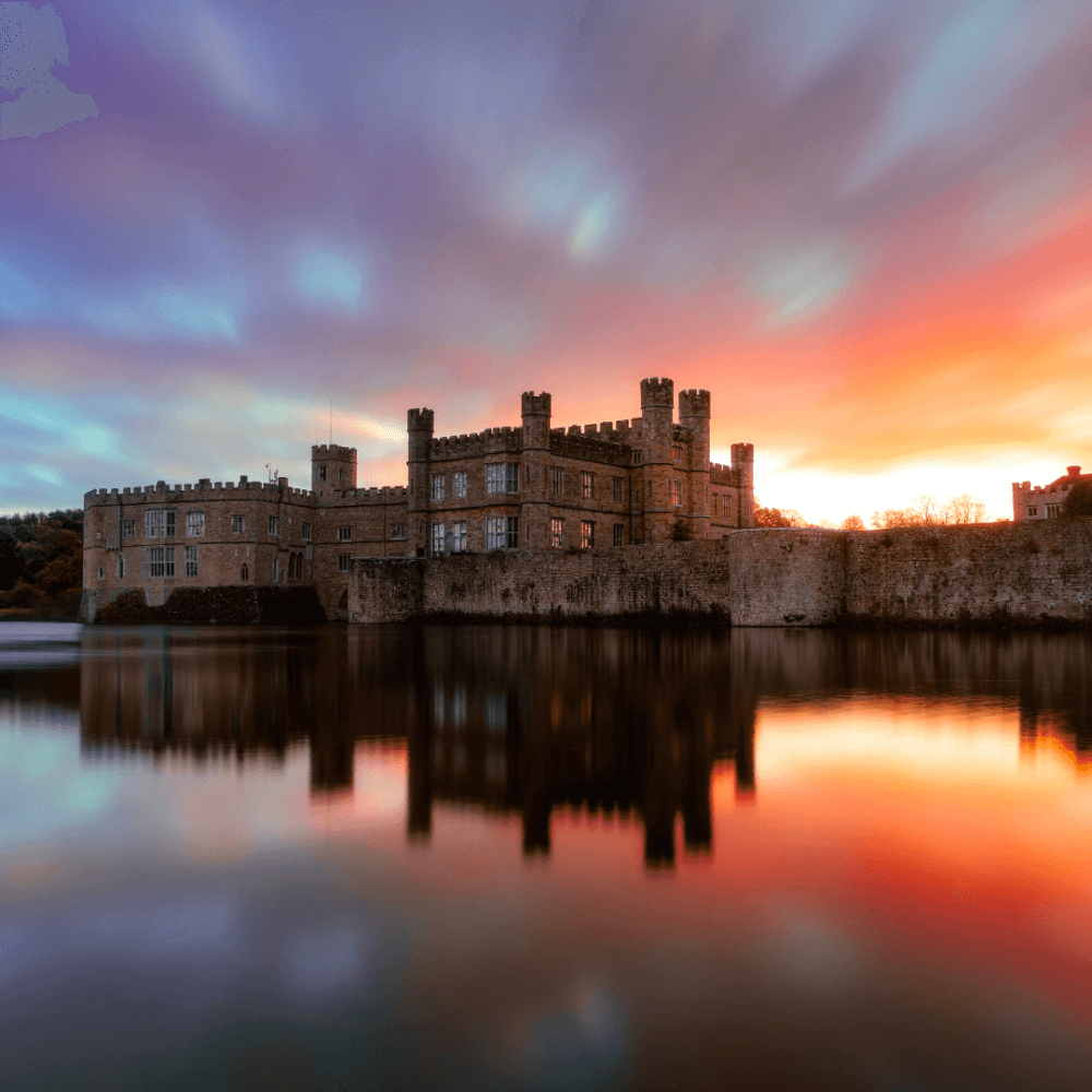 A grand castle with towers and turrets reflected in the water under a vibrant, colorful sunset sky. - Home Instead