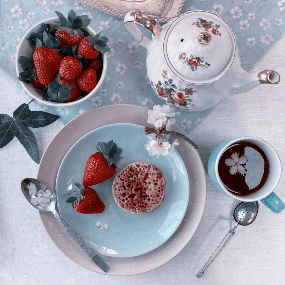 Breakfast scene with strawberries, a crumpet, tea in a floral teapot, and coffee in a blue cup. - Home Instead