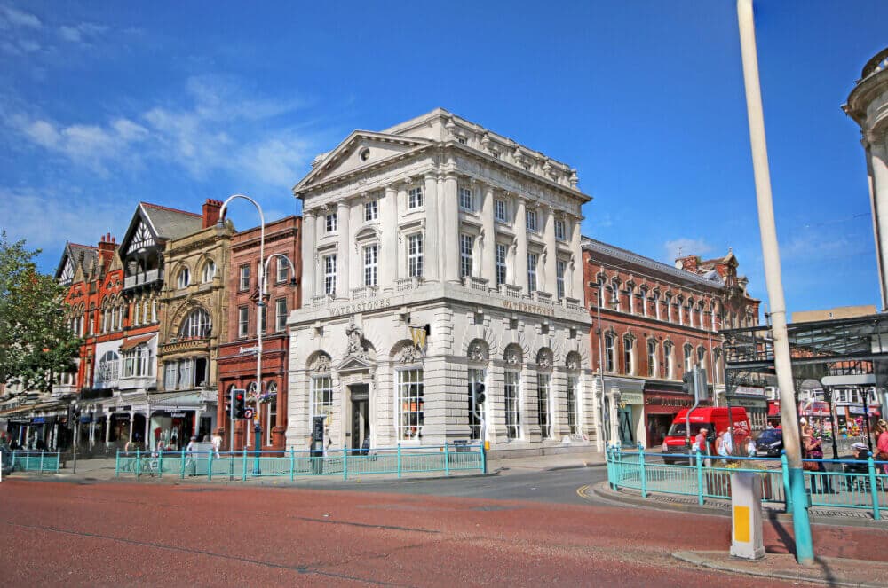 Historic building with ornate architecture along a vibrant city street, featuring shops and a red double-decker bus. - Home Instead