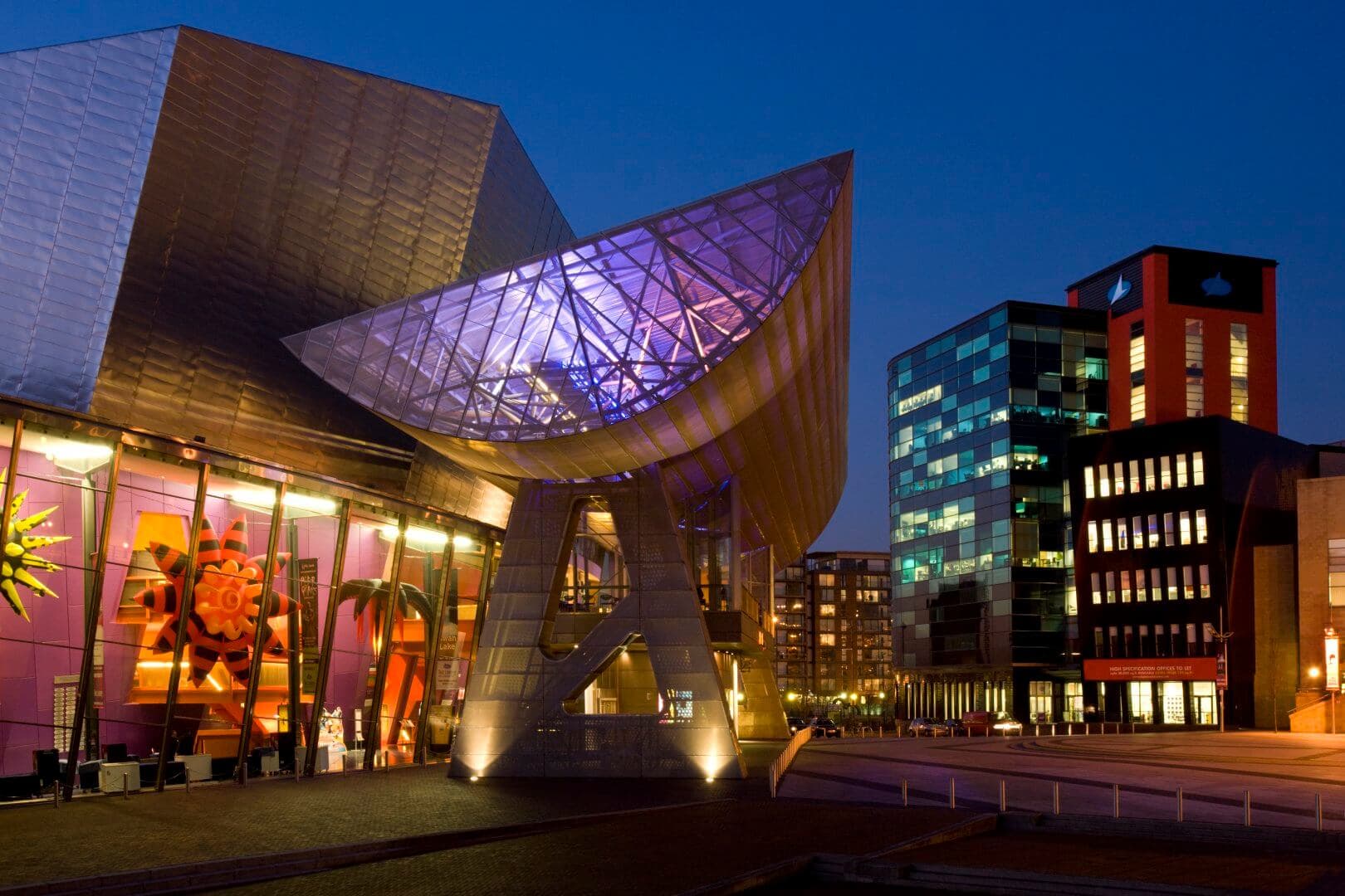 Modern architectural building with colorful lighting and glass structures at twilight, surrounded by office buildings. - Home Instead