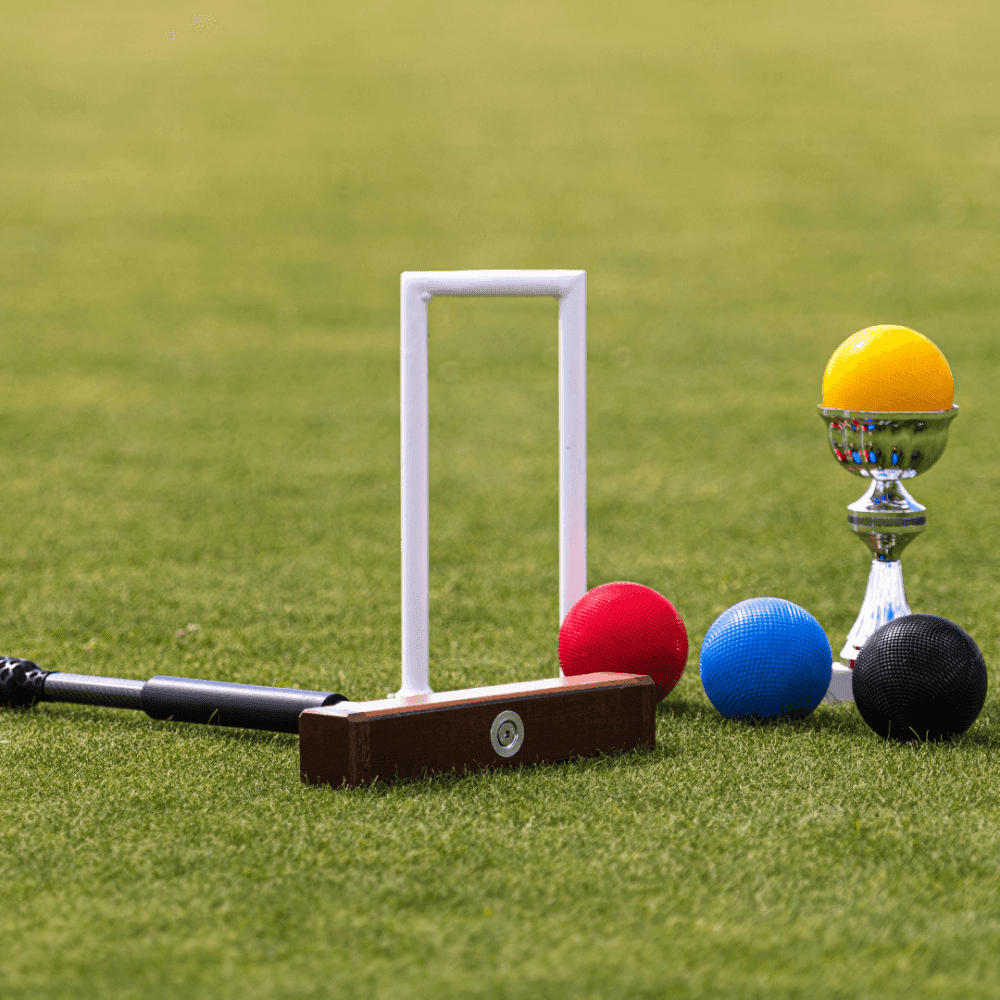 Croquet set with colored balls, a mallet, a wicket, and a trophy on a green lawn. - Home Instead