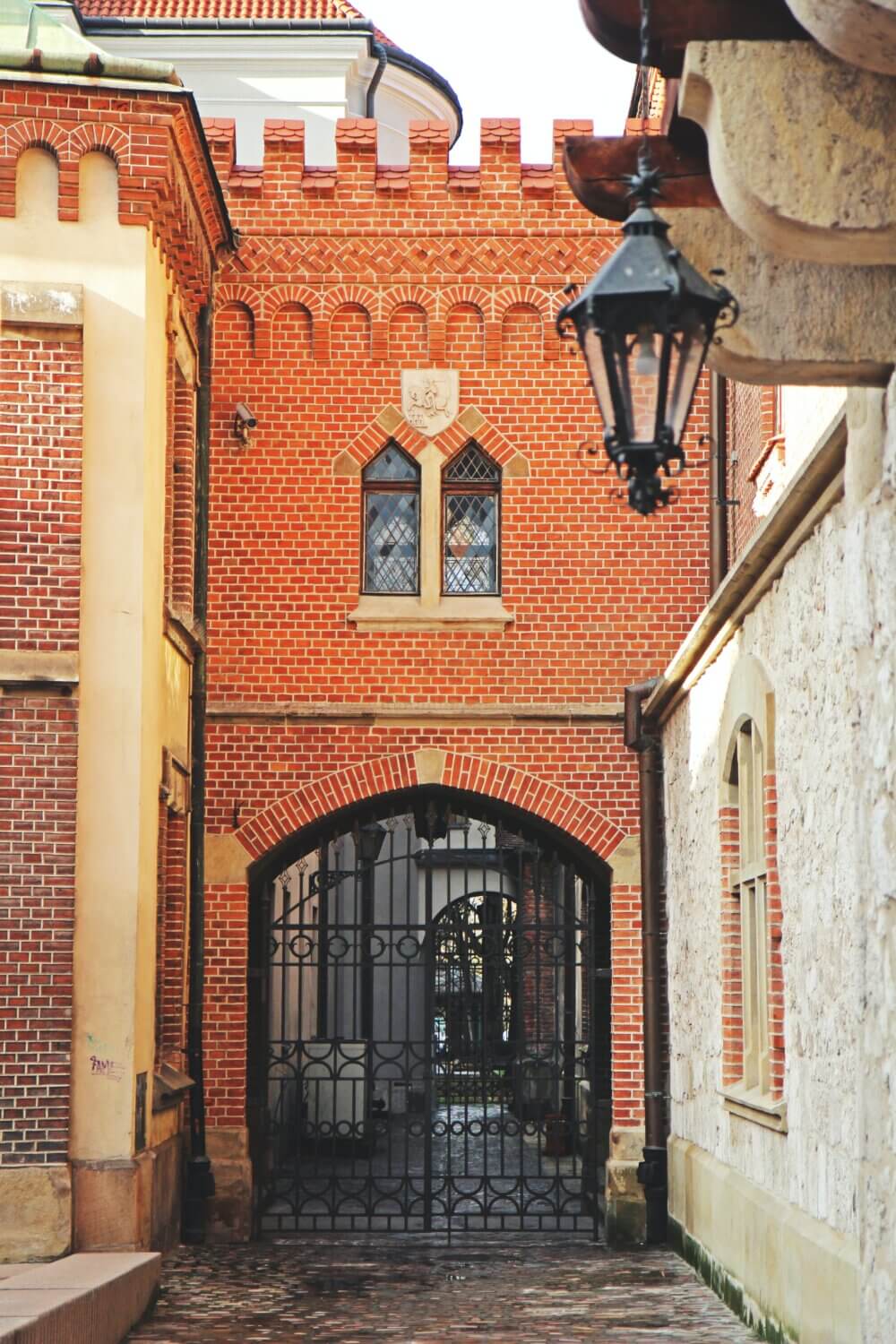 Narrow alley with a brick archway, medieval architecture, and metal gate under an ornate lantern. - Home Instead