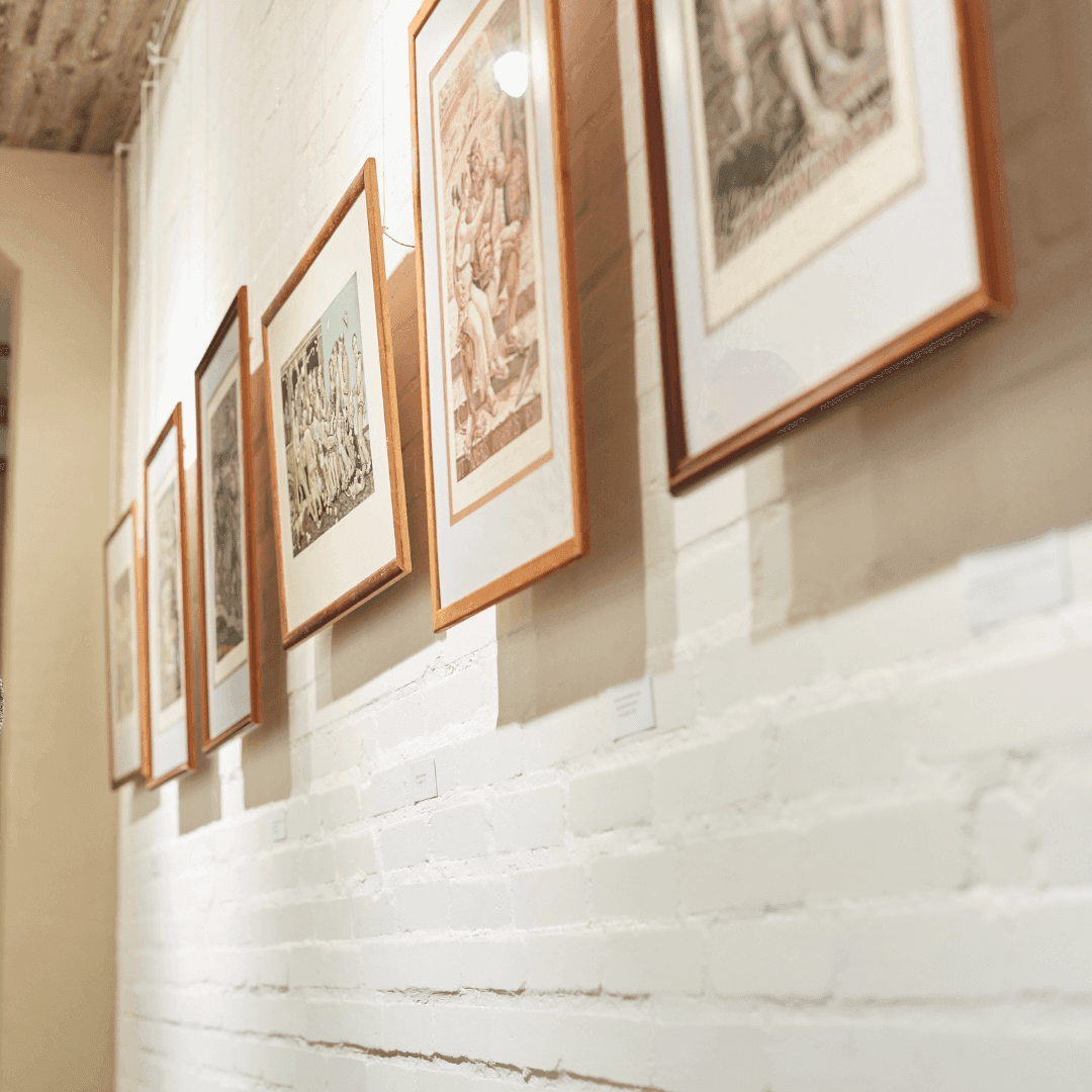 A row of framed pictures displayed on a white brick wall in an art gallery. - Home Instead