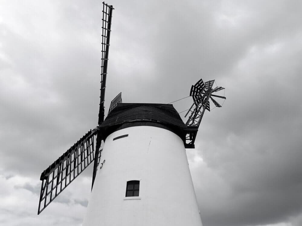 A white windmill with large blades under a cloudy, overcast sky. - Home Instead