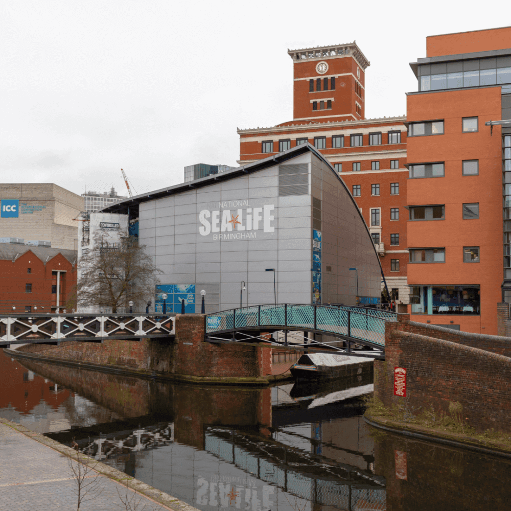 National SEA LIFE Centre in Birmingham, with a canal and bridge in the foreground, surrounded by various buildings. - Home Instead
