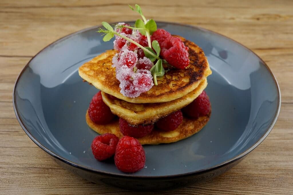 Stack of pancakes topped with fresh raspberries and greens on a blue plate. - Home Instead