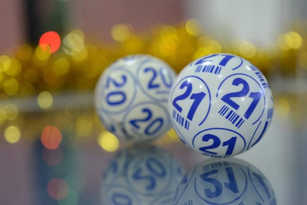 Close-up of lotto balls numbered 20 and 21 with a blurred background decorated with gold tinsel and colorful lights. - Home Instead