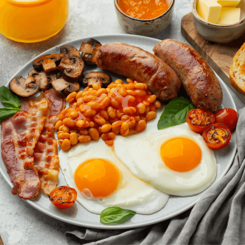 A full English breakfast with eggs, sausages, bacon, beans, tomatoes, and mushrooms on a plate. - Home Instead