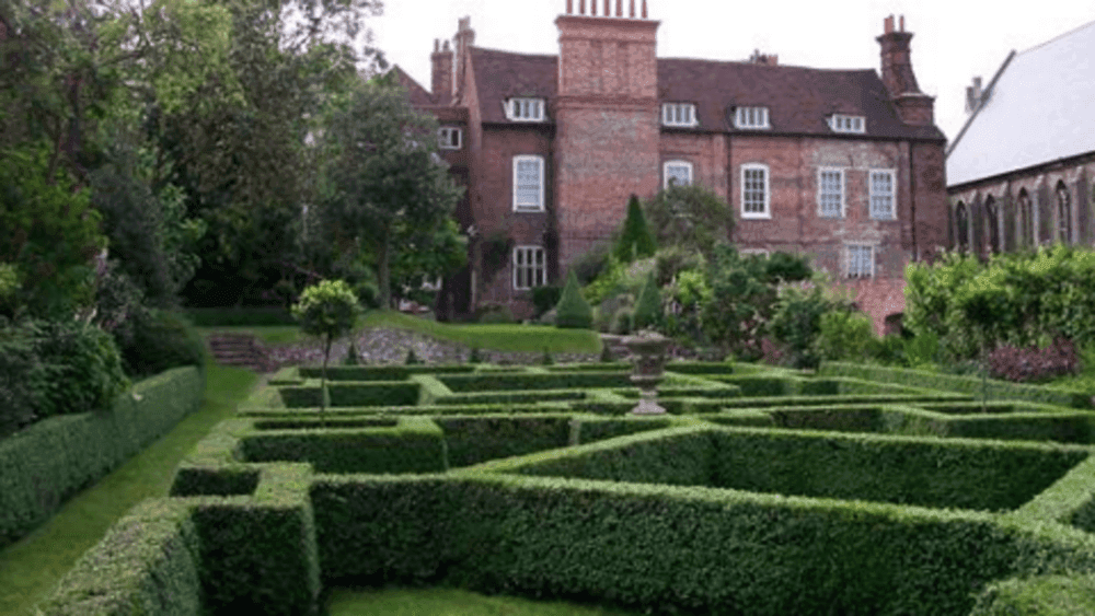 A historic brick building with chimneys behind a manicured hedge maze in an ornate garden. - Home Instead