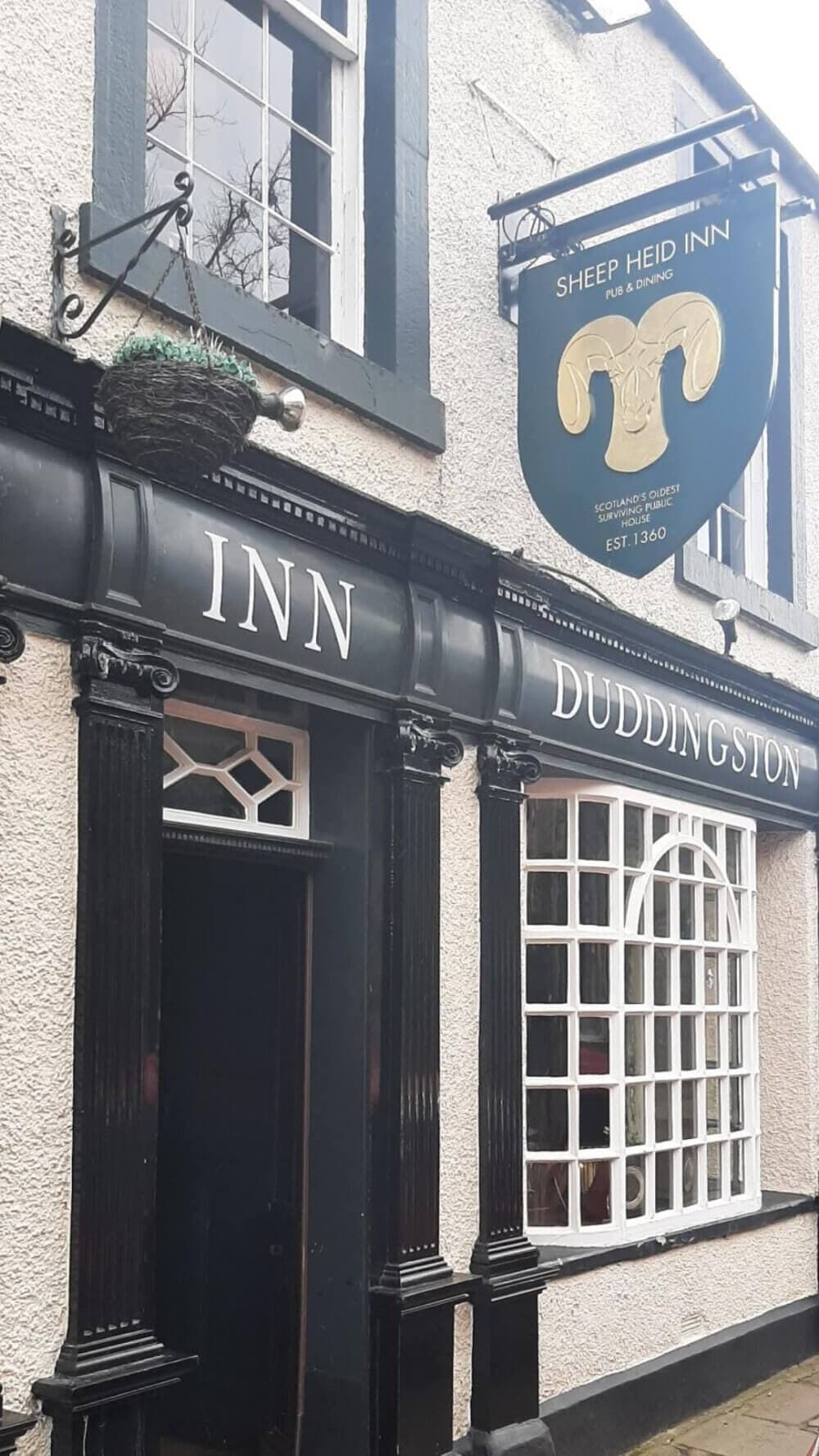 Exterior of the Sheep Heid Inn in Duddingston, featuring black trim and a green sign with a golden sheep's head. - Home Instead