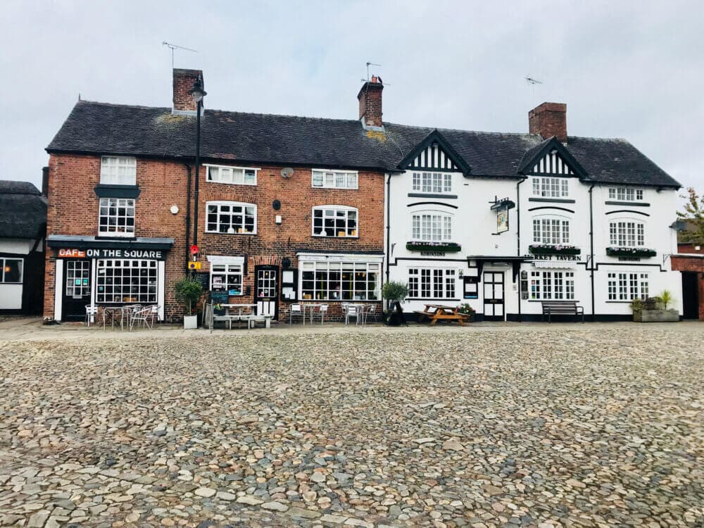Historic brick and timber-framed buildings with a café on a cobblestone square; outdoor seating visible. - Home Instead