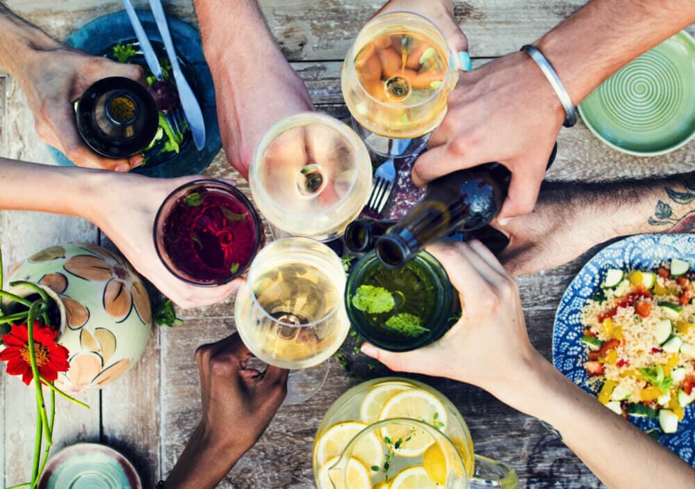 Friends toasting with various drinks around a wooden table set with food, capturing a celebration moment from above. - Home Instead